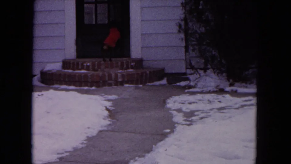 The dog reaches the front entry of the white-sided house, standing near the dark door above brick steps in 1964 Evanston footage.