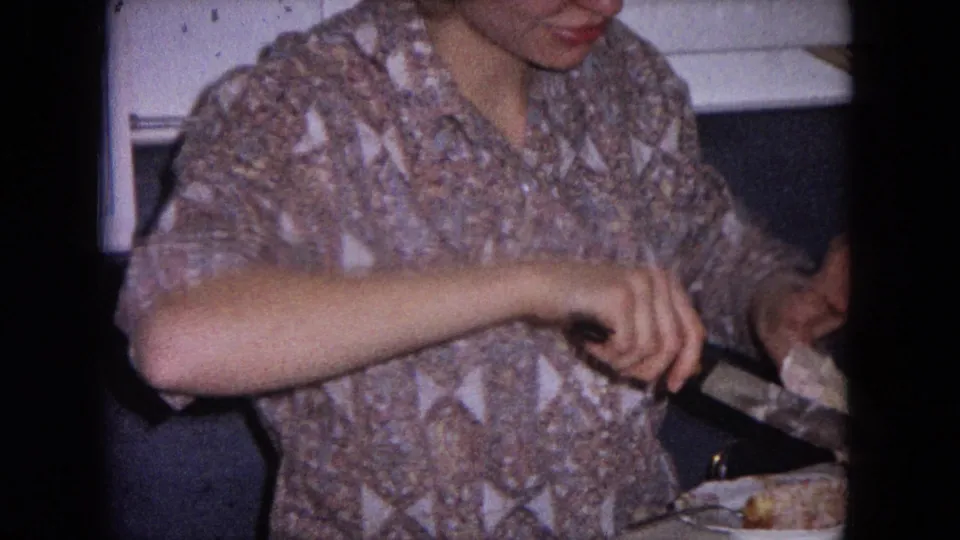 The woman continues cutting or serving the white iced cake in the Evanston home kitchen, framed tightly by 8mm film edges.