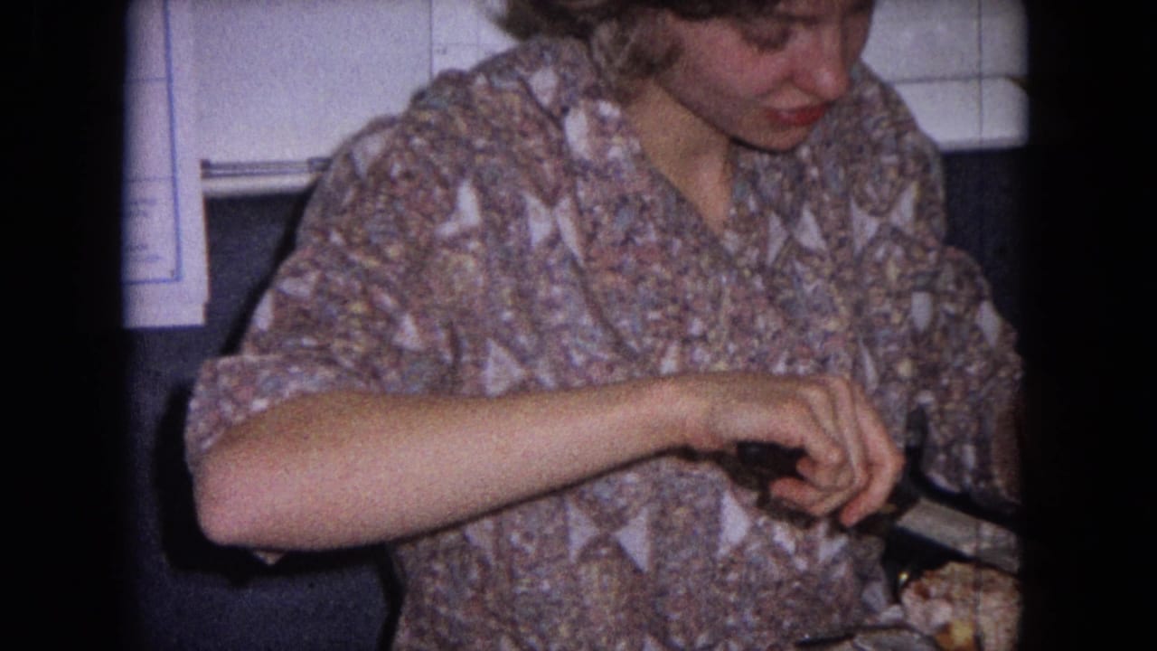 Adult woman in a patterned blouse cuts food at a table indoors.