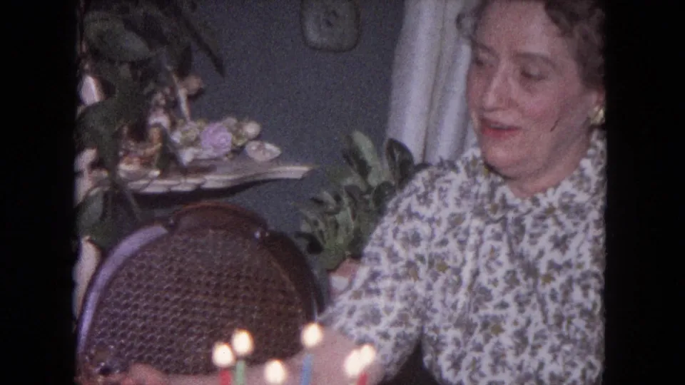 The woman appears to look down toward the candlelit birthday cake during the 1964 Evanston home-movie scene.