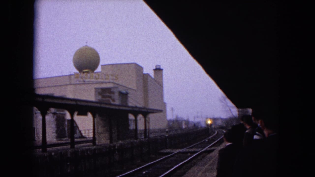 Train tracks curve past a station platform with a dome-topped building and a distant headlight.