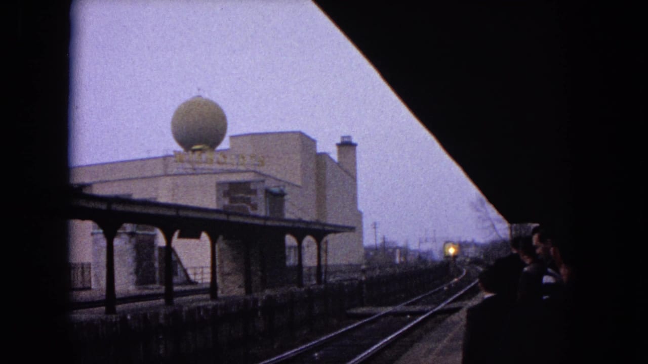 Station platform and tracks seen through dark framing as a train light approaches in the distance.