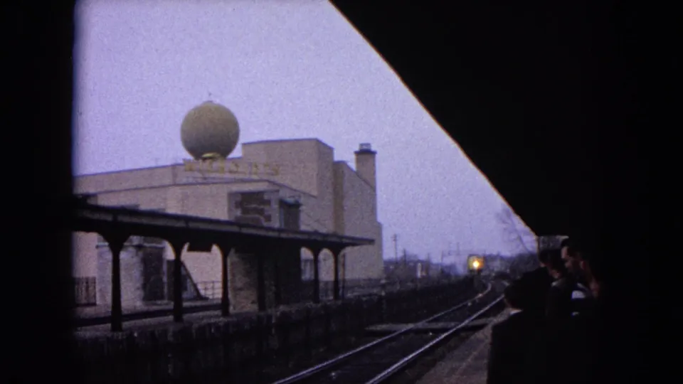 Evanston, Illinois station view with tracks, platform shelter, waiting people, distant train headlight, and spherical rooftop dome.