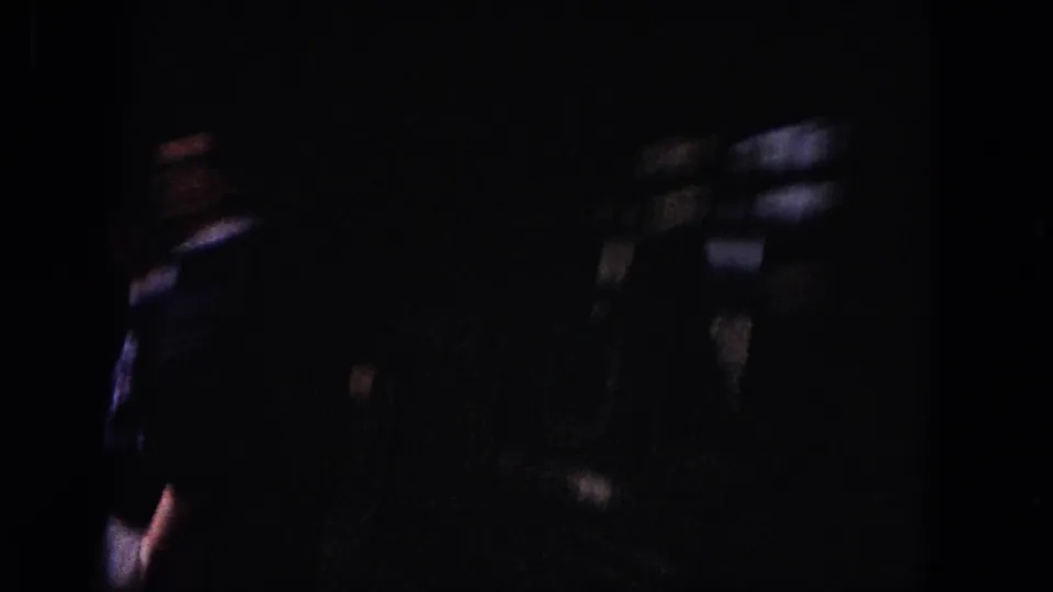 Low-light 8mm frame from the train-side viewpoint, with indistinct passenger silhouettes and dark reflective areas dominating the view.