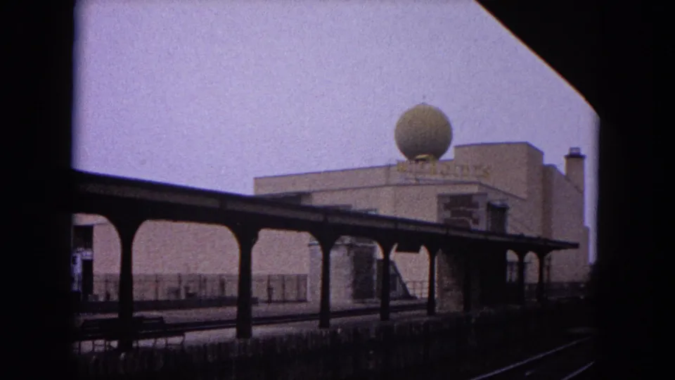 1964 Evanston station scene with canopy supports, rail lines, platform edge, and the large spherical rooftop dome on a nearby building.