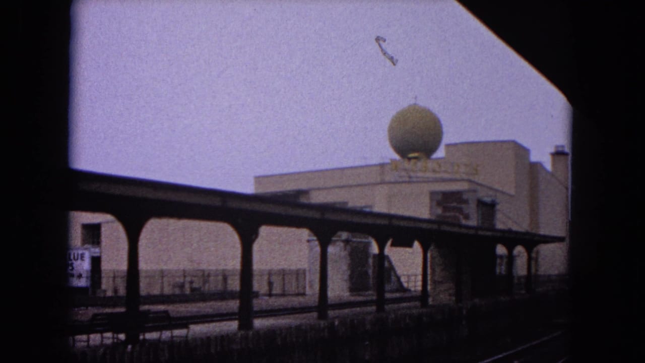 Covered station platform seen across tracks with a rooftop dome above a building.