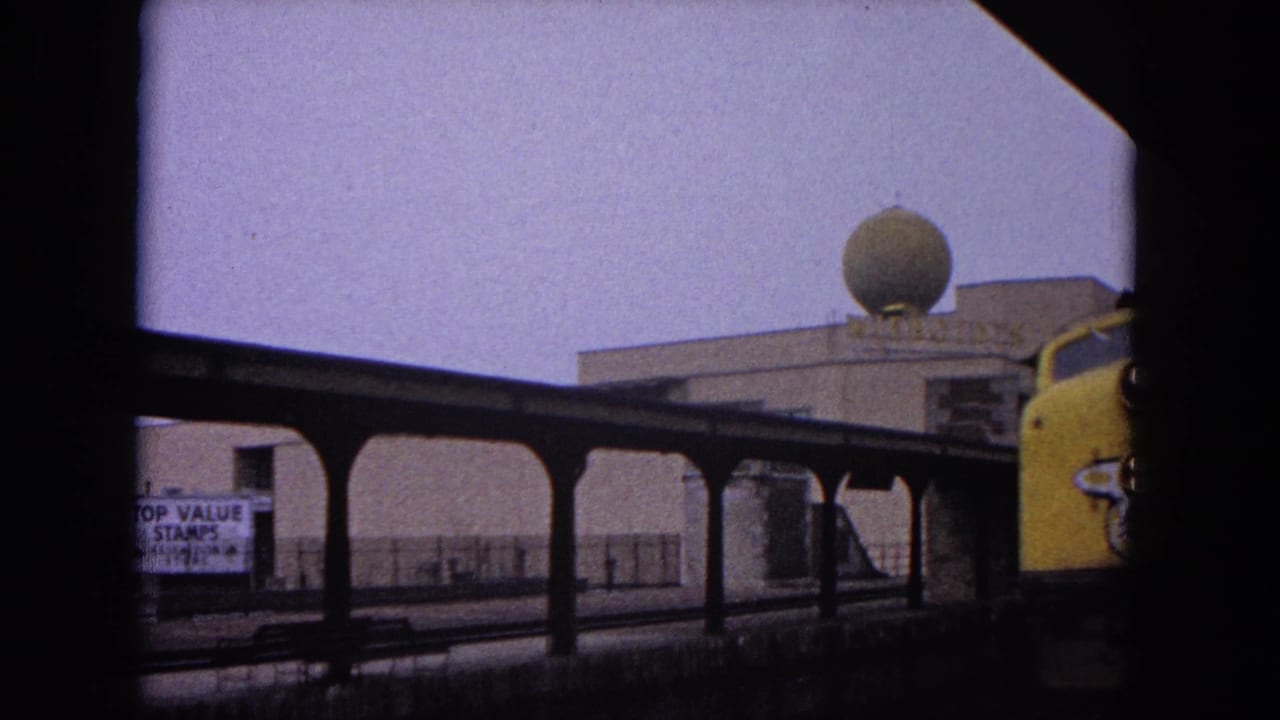 Yellow train enters the station beside a covered platform and domed building.