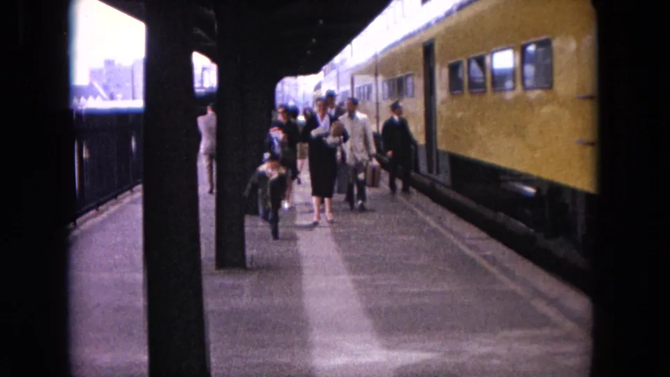 Passengers stand and walk along the Evanston station platform beside a yellow railcar, with city buildings visible beyond.