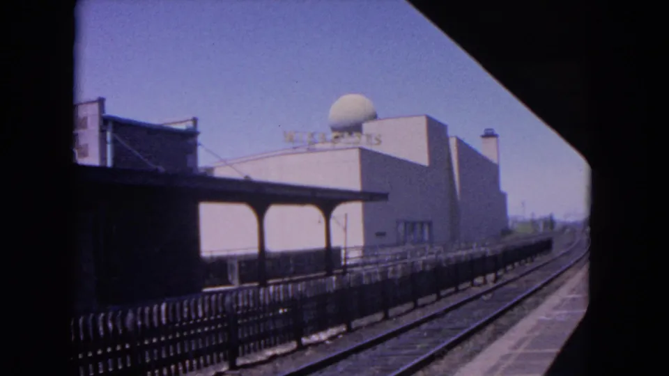 1964 Evanston station view showing empty tracks, platform fencing, canopy, dome-topped building, and visible Wisconsin signage.