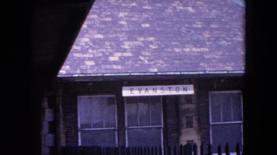 Evanston station building with the EVANSTON sign visible, seen through a dark train-side frame in 1964 home-movie footage.