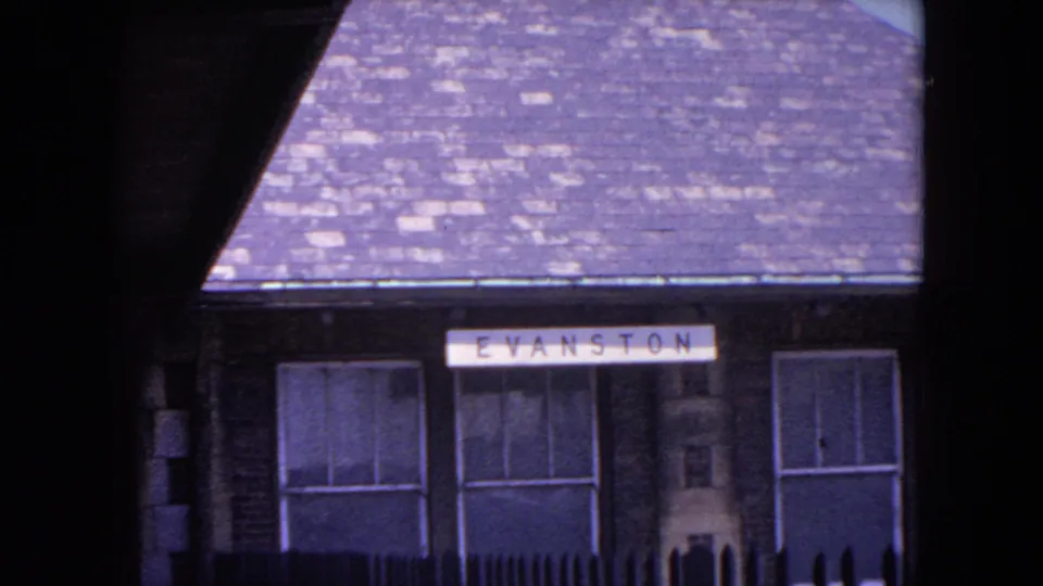 Close 1964 8mm view of the Evanston station facade with sign, roof, windows, and trackside architectural details.