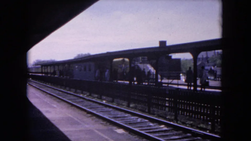 1964 Evanston railway station view with tracks, a covered platform, and passengers waiting as a train approaches.