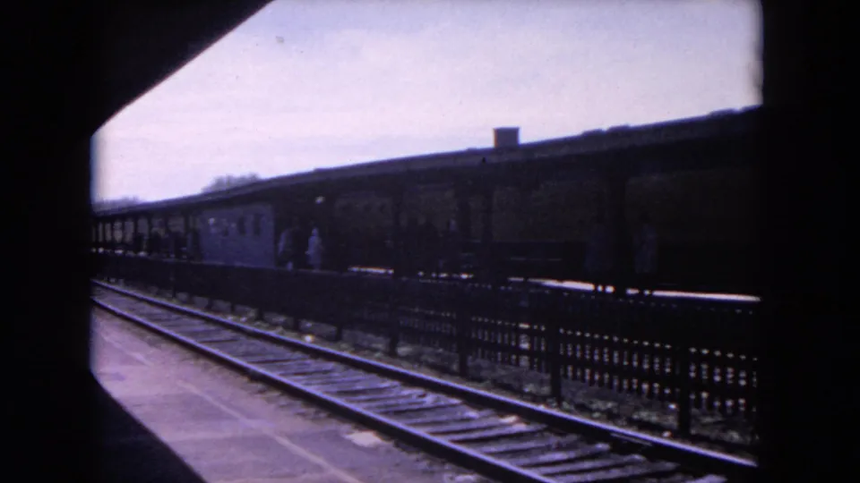 A yellow rail car passes through the Evanston station view, framed by tracks, fencing, and the platform shelter.