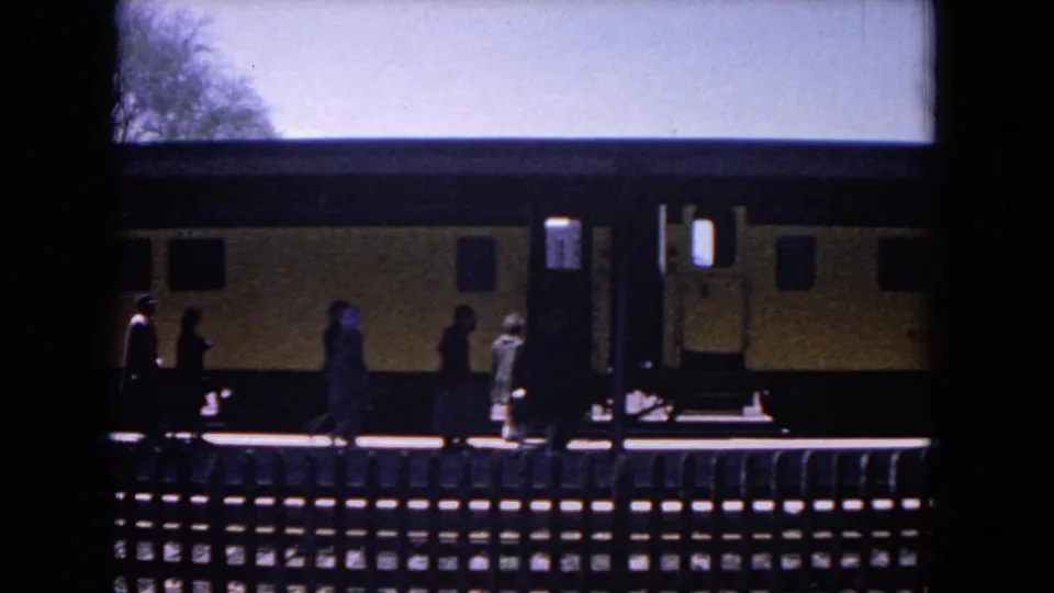 Several passengers stand beside a yellow train car at the Evanston station platform in 1964 home-movie footage.