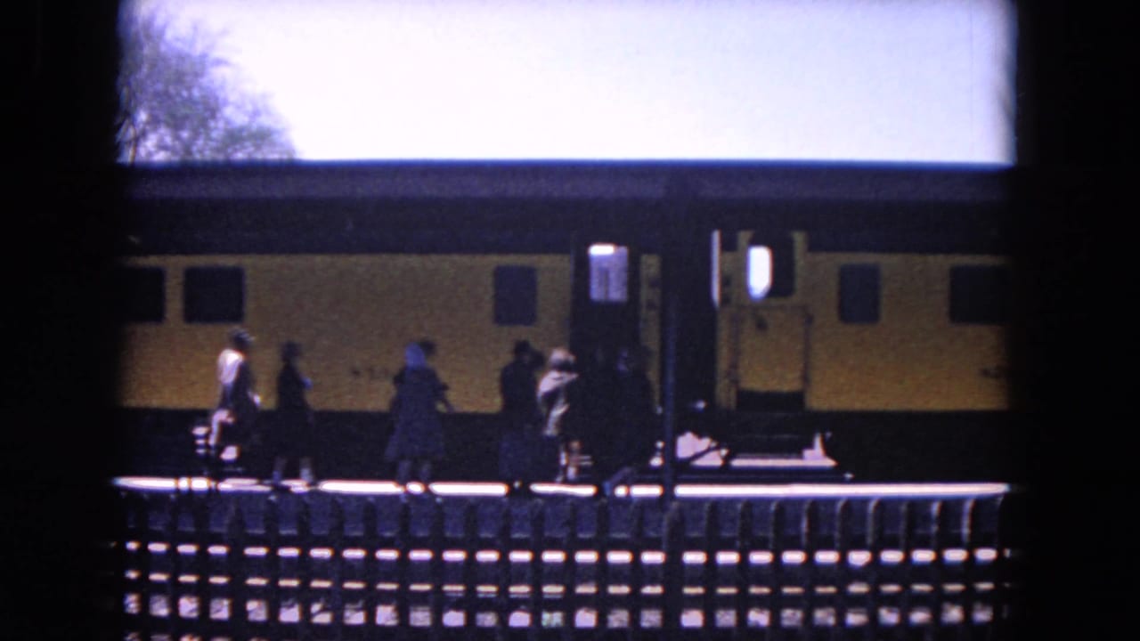 Passengers walk along a platform beside a yellow-and-black train seen through a dark foreground frame.