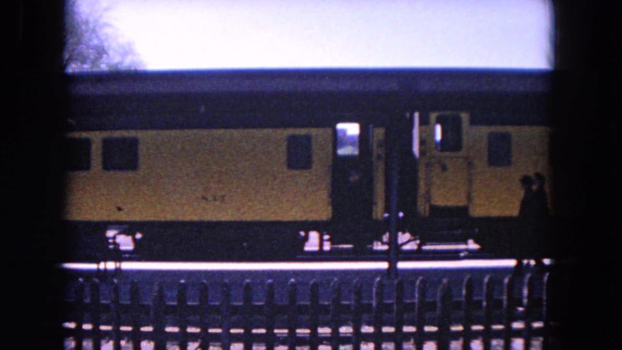 A person appears near the open doorway of a yellow train on an Evanston platform, filmed on 8mm in 1964.