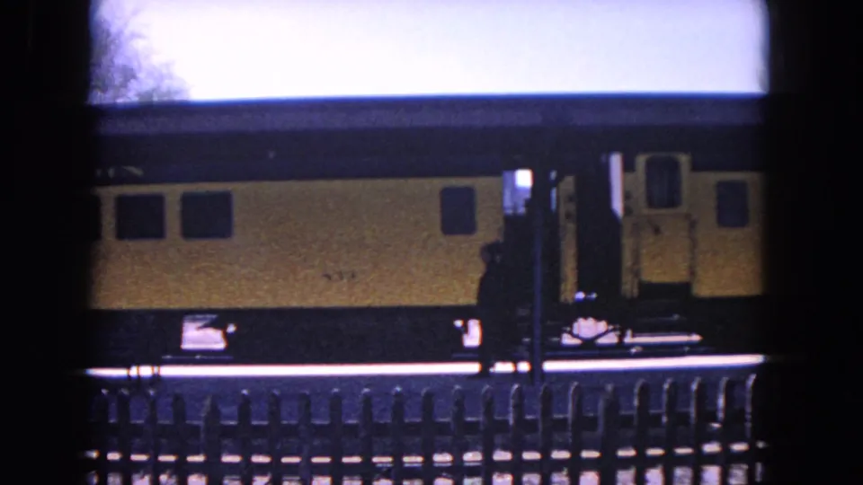 A silhouetted person walks along the platform beside the yellow train in this 1964 Evanston 8mm frame.