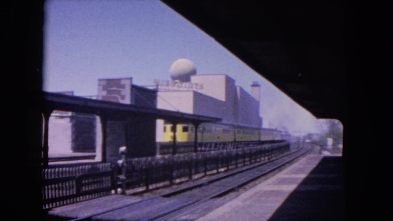 Yellow electric train beside an elevated station platform with a rooftop dome building in the background.