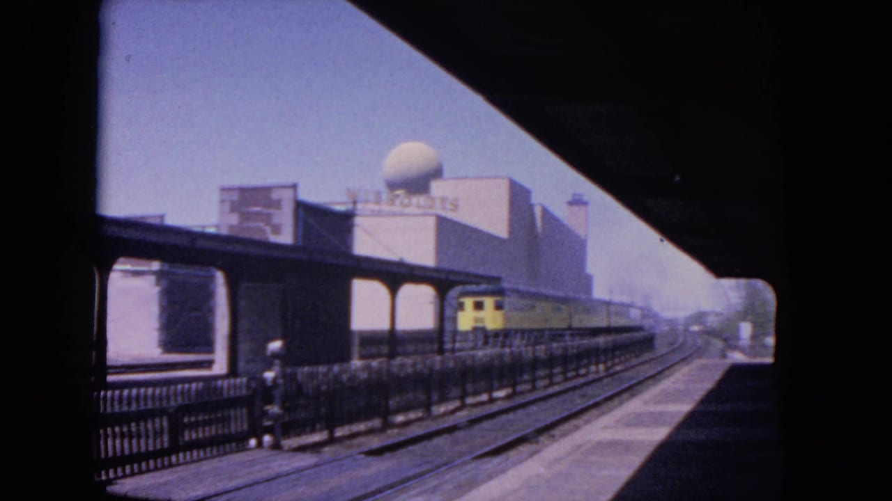 1964 Evanston station view from a moving train, with a yellow electric train, platform canopy, tracks, and a signed building with rooftop dome.