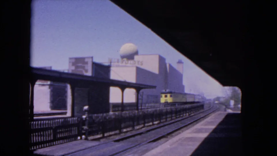 1964 Evanston electric rail scene with the yellow train farther down the platform, tracks leading forward, and the dome-topped building behind.