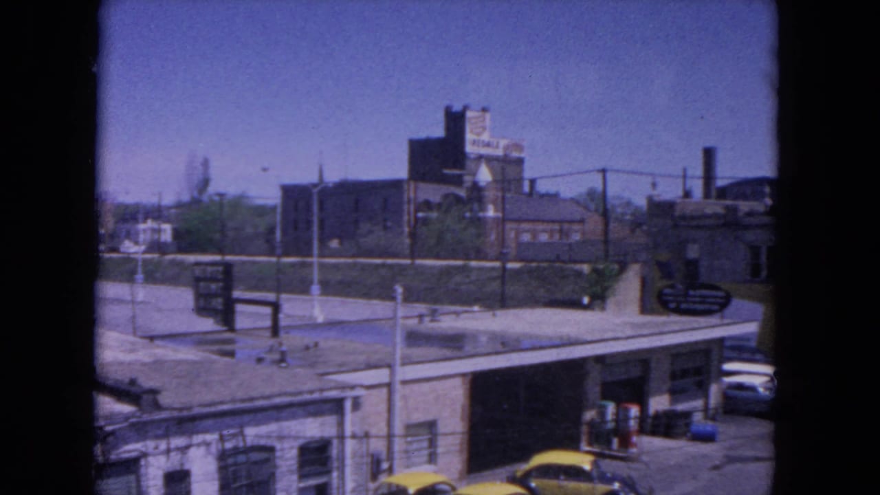 View from a station area toward industrial buildings, parked cars, and platform structures.
