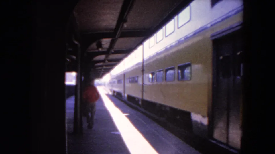 The yellow passenger train continues past the covered platform while the man in red moves away from the camera in Evanston.
