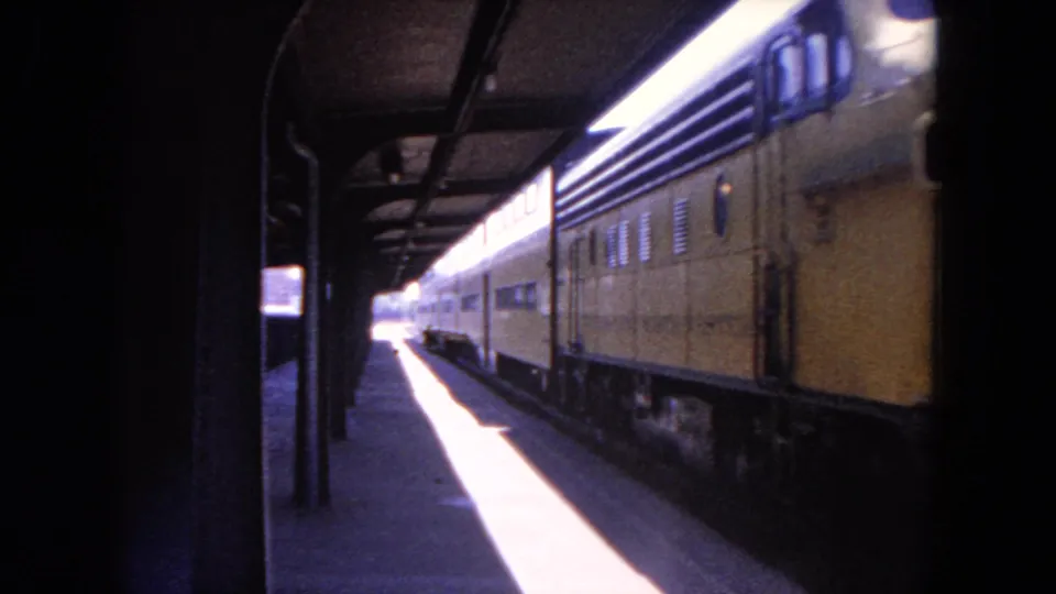 A yellow locomotive or passenger car passes under the Evanston platform canopy with windows, vents, and rail-side shadows visible.