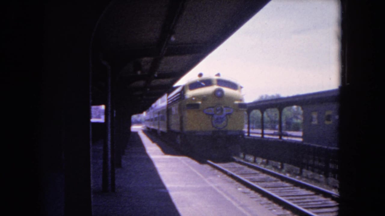 1964 Evanston station view with the yellow train moving along the platform and a darker passenger car visible on the adjacent track.