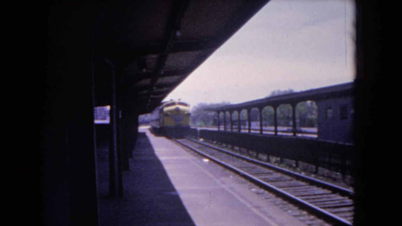 Covered rail platform with tracks, rail cars, and a train in the distance.