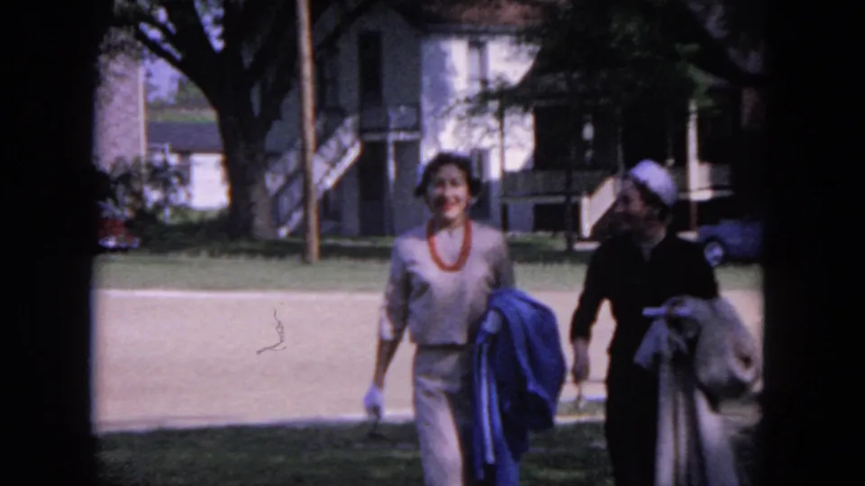 Near the end of the 1964 Evanston clip, two women approach the camera carrying coats on a residential lawn.