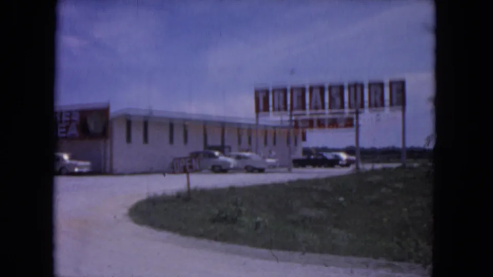 1964 Evanston exterior with a large Treasure City roadside sign, parked cars, open sign, and low storefront building.