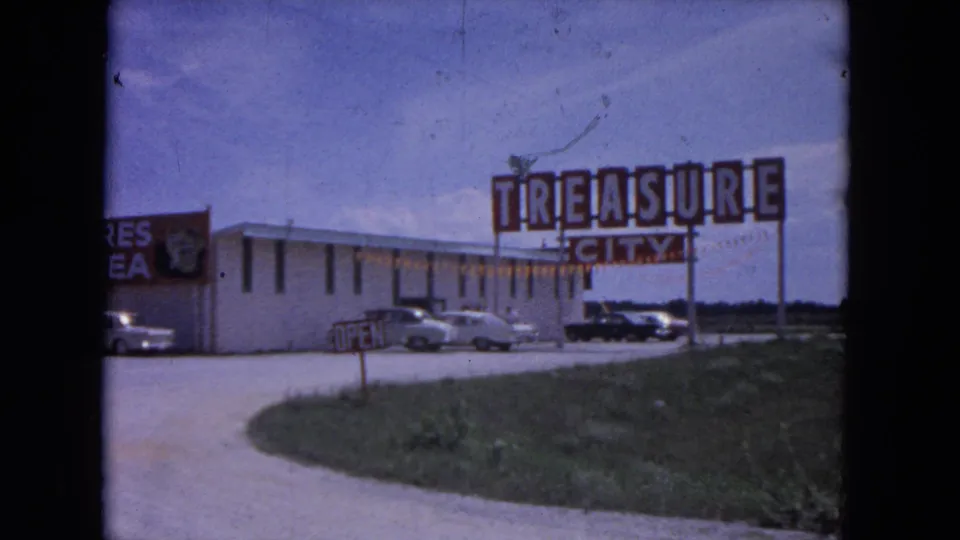 Clearer 1964 Evanston frame showing the large Treasure City sign and Treasures from the Sea sign beside parked mid-century cars.