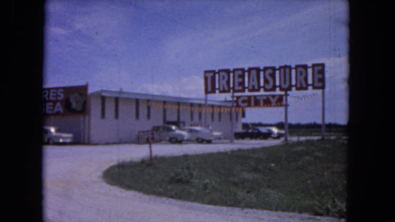 Roadside tourist shop with large Treasure City sign, parked cars, and an open driveway.