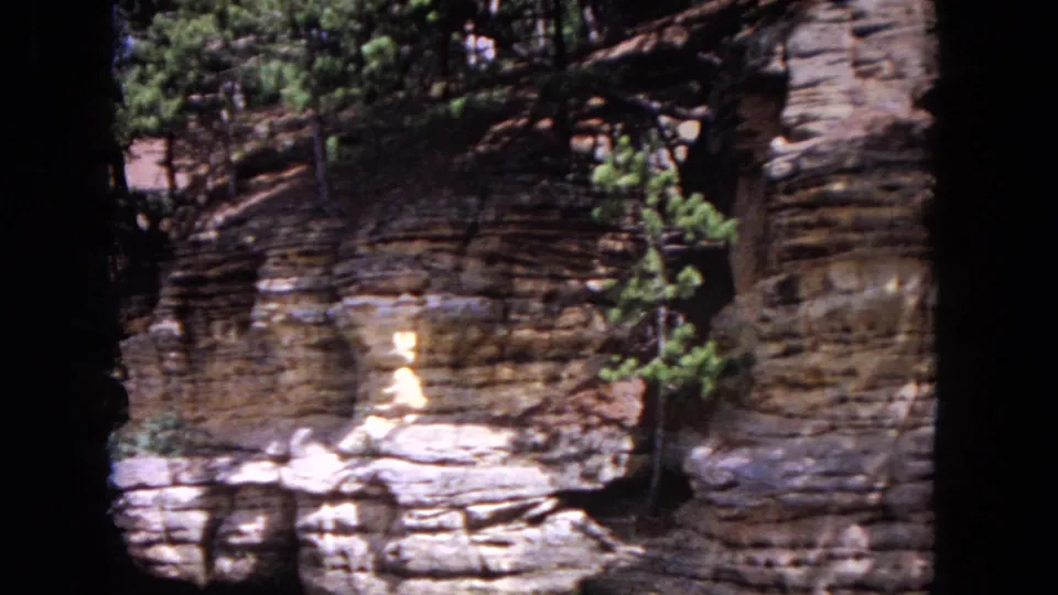 End of the 1964 Evanston 8mm pan showing weathered riverbank ledges, evergreen branches, water, and heavy film-frame borders.