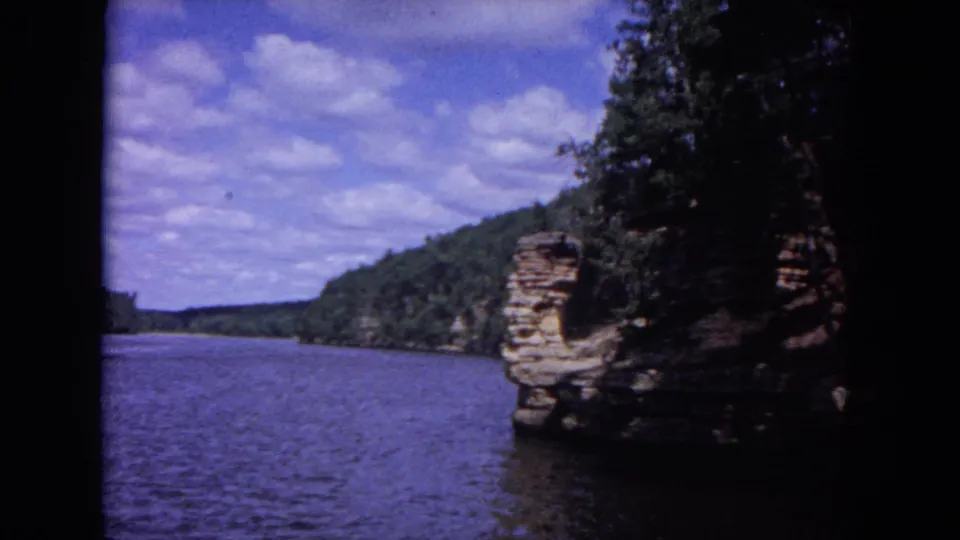 1964 8mm view of a lake near Evanston, Illinois, with trees and stratified rocky cliffs in bright daylight.