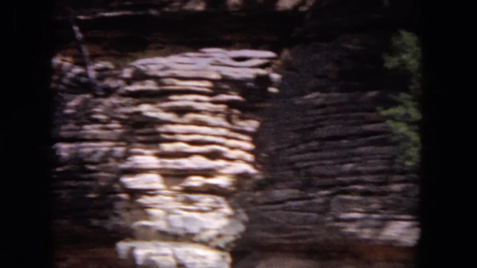 Close 8mm frame of stratified rock ledges along the Evanston lakeside, partly shaded with trees at the edge.