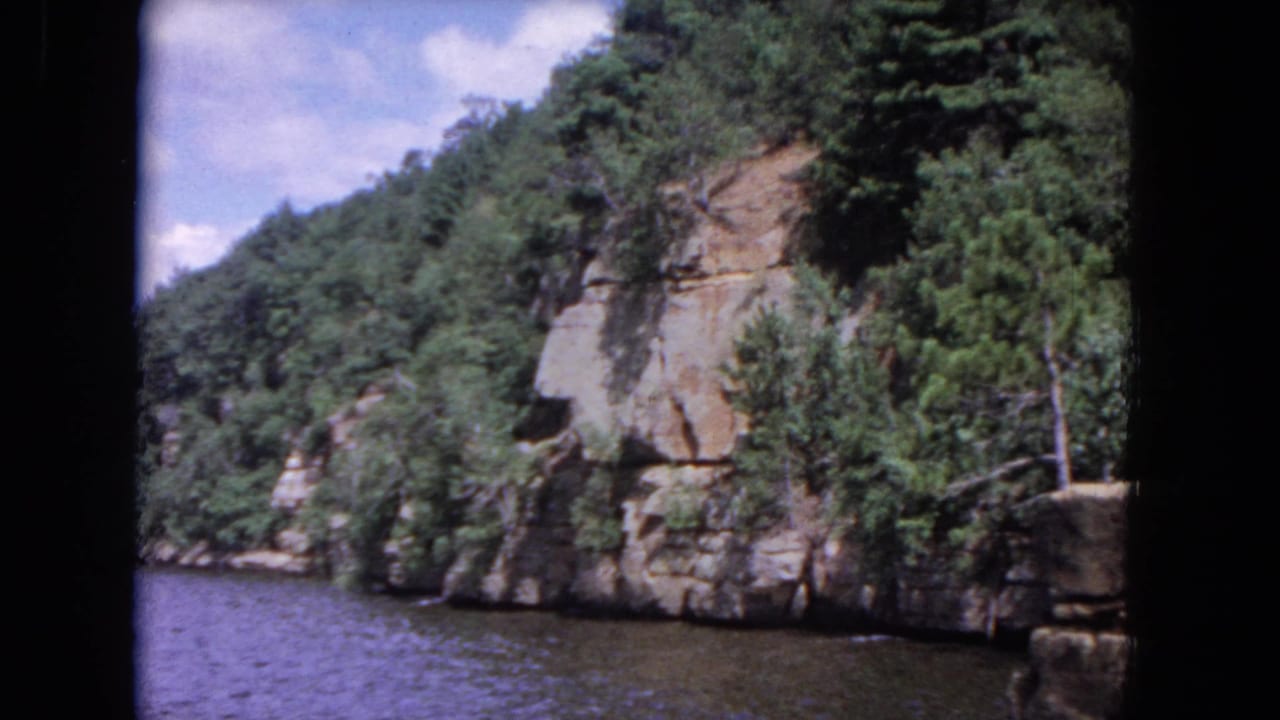 Rocky river cliff with trees and shrubs above rippled water.