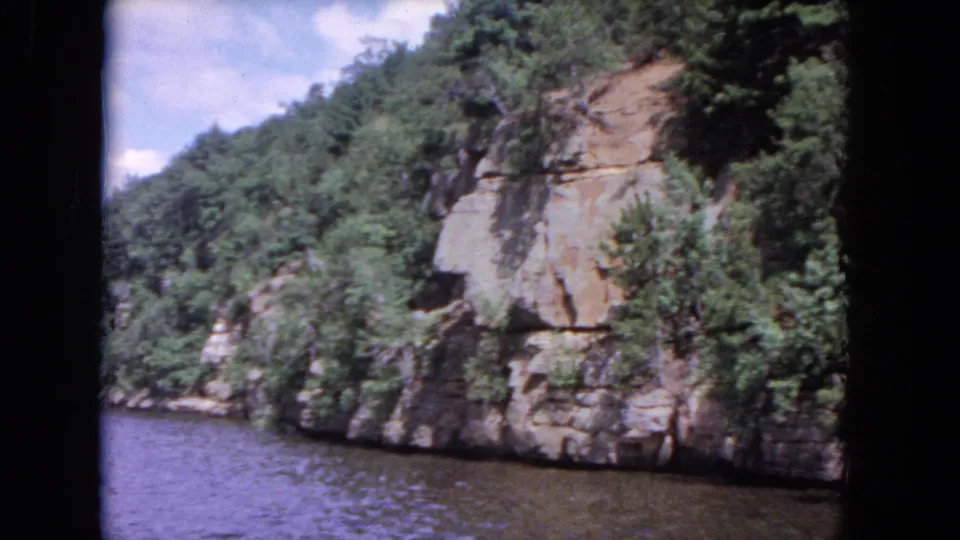 Vintage 8mm frame showing rippled water below a rugged, green-covered cliff, consistent with the supplied 1964 Evanston clip metadata.