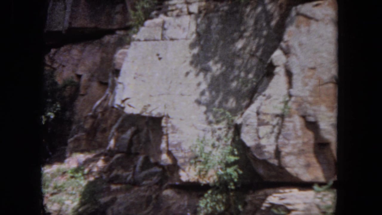 Rock wall and trees beside a dark river, seen through 8mm film frame edges.