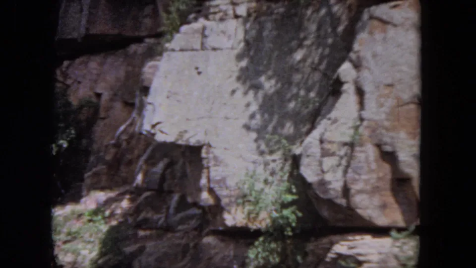 Cataloged 1964 8mm footage shows a sunlit rock face with trees beside a slow river in Evanston, Illinois.