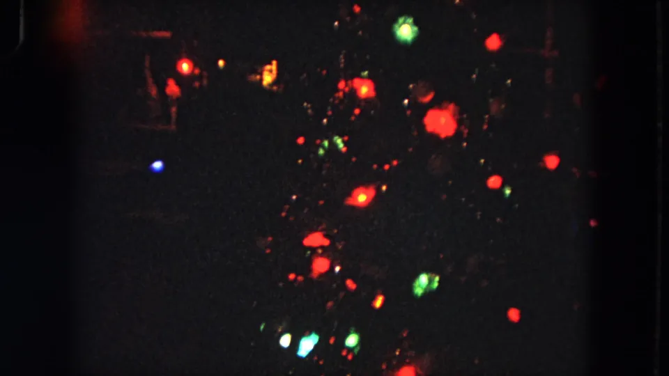 1964 8mm home-movie frame showing scattered colored lights in a dark Evanston night scene, with strong grain and soft focus.