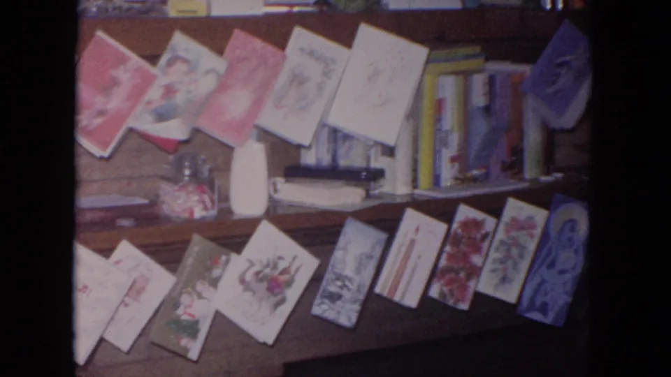 1964 Evanston home-movie frame showing Christmas cards on a wooden fireplace mantel with books, a candy jar, and small household objects.