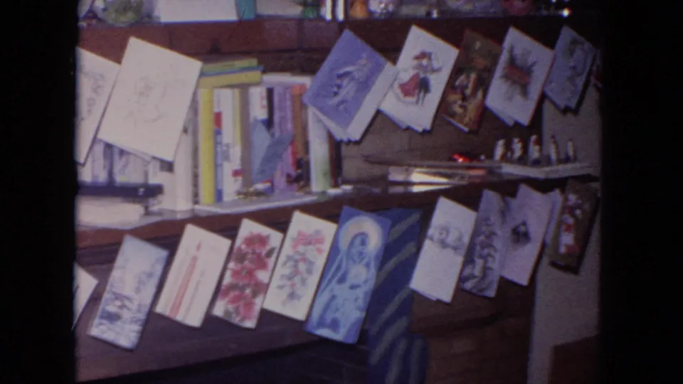 1964 Evanston 8mm frame showing a private mantel display with holiday cards, books, small figures, and a blue folded paper decoration.