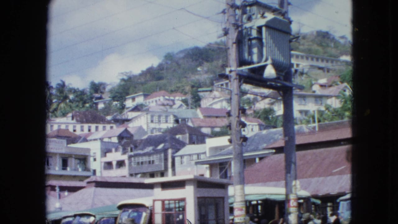 A bright 8mm town view shows hillside houses, red roofs, utility wires, older vehicles, and pedestrians near the lower edge.