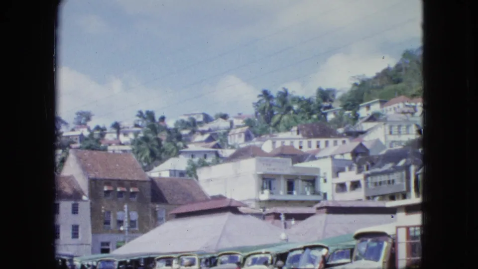 A wider 8mm view shows a hillside town, palm trees, rooflines, older vehicles at the bottom, and a foreground building edge.