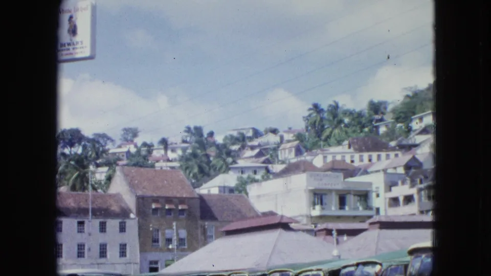 A shaded frame looks toward hillside houses, palm trees, tiled roofs, and lower street buildings in archival 8mm footage.