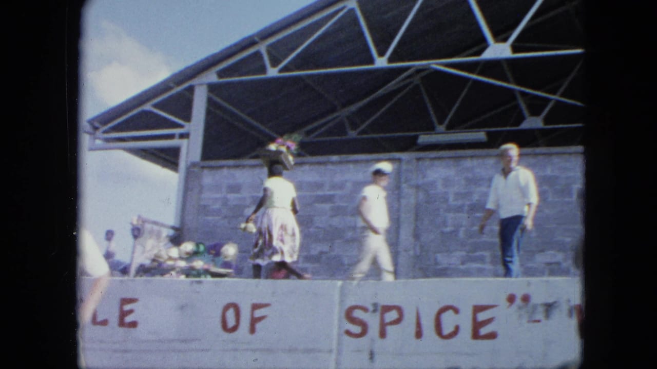 People walk on a raised stage under a metal roof behind a painted sign.