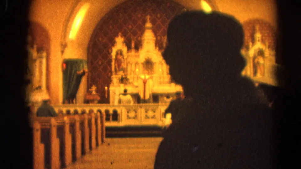 Soft 1964 8mm frame showing a foreground congregant silhouette and ornate altar inside a Harvard, Illinois church.