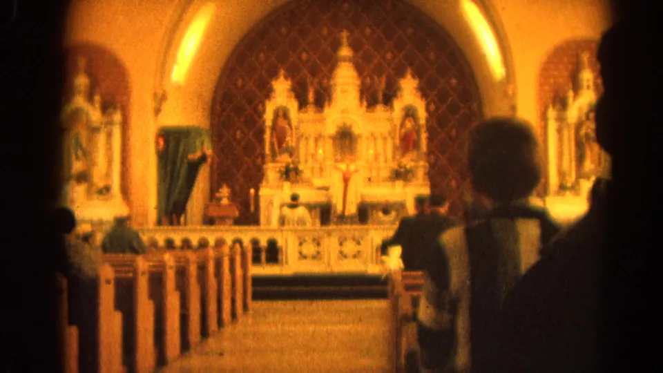 Final 8mm frame of a Catholic Mass, showing parishioners from behind and a bright altar inside a Harvard, Illinois church.
