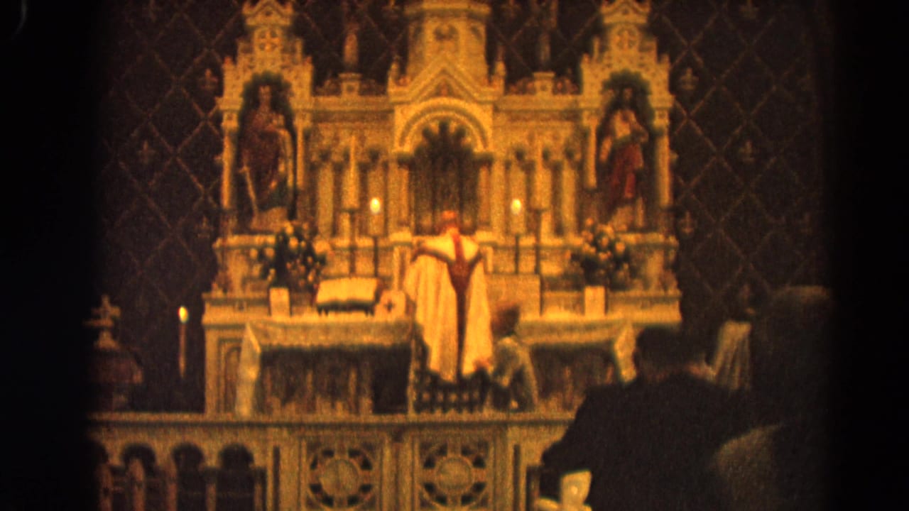 Priest in vestments stands at an ornate church altar with candles and statues.